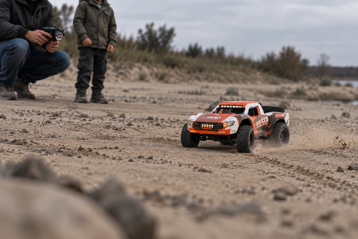 Un adulte et un enfant pilotent le trophy truck Rapid, une radiocommande chacun