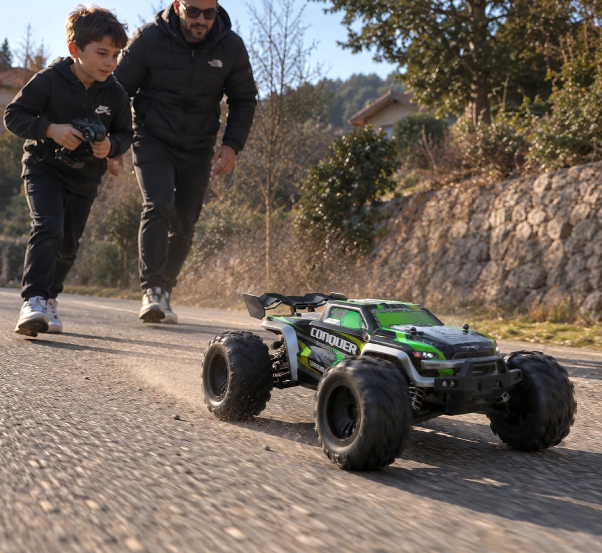 Un enfant à la radiocommande et un adulte derrière lui, suivant le Conquer 4×4 1/16 vert sur une route